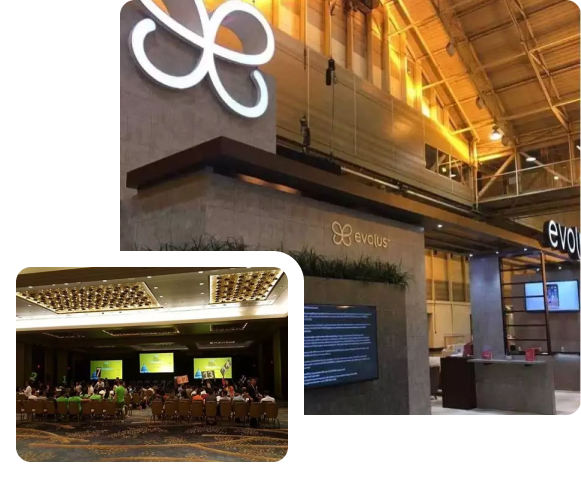 This image features two views of a corporate event at a venue branded with the "evolus" logo. The larger image shows a modern reception area with high ceilings, ambient lighting, and the "evolus" logo prominently displayed on a stone wall. The area is sleek and professional, designed for hosting business events. The smaller inset image depicts an event room with attendees seated in rows, facing a stage with multiple screens displaying presentations. The room is well-lit and spacious, indicating a conference or seminar setup. Overall, the photos convey a sophisticated and professional event environment.